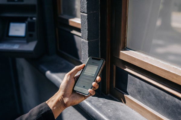 Hand hält Smartphone in der Nähe des Fensters eines Geldautomaten (ID#5)
