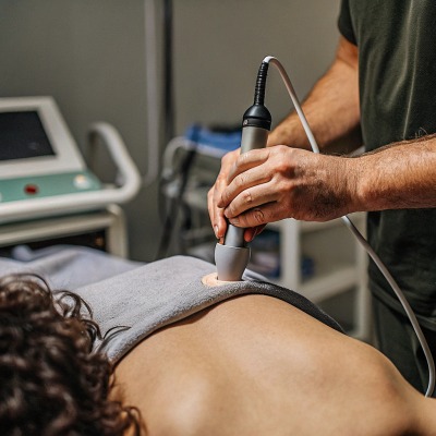 Terapia en curso Terapeuta usando un dispositivo de onda de choque en la espalda del paciente (ID#3)
